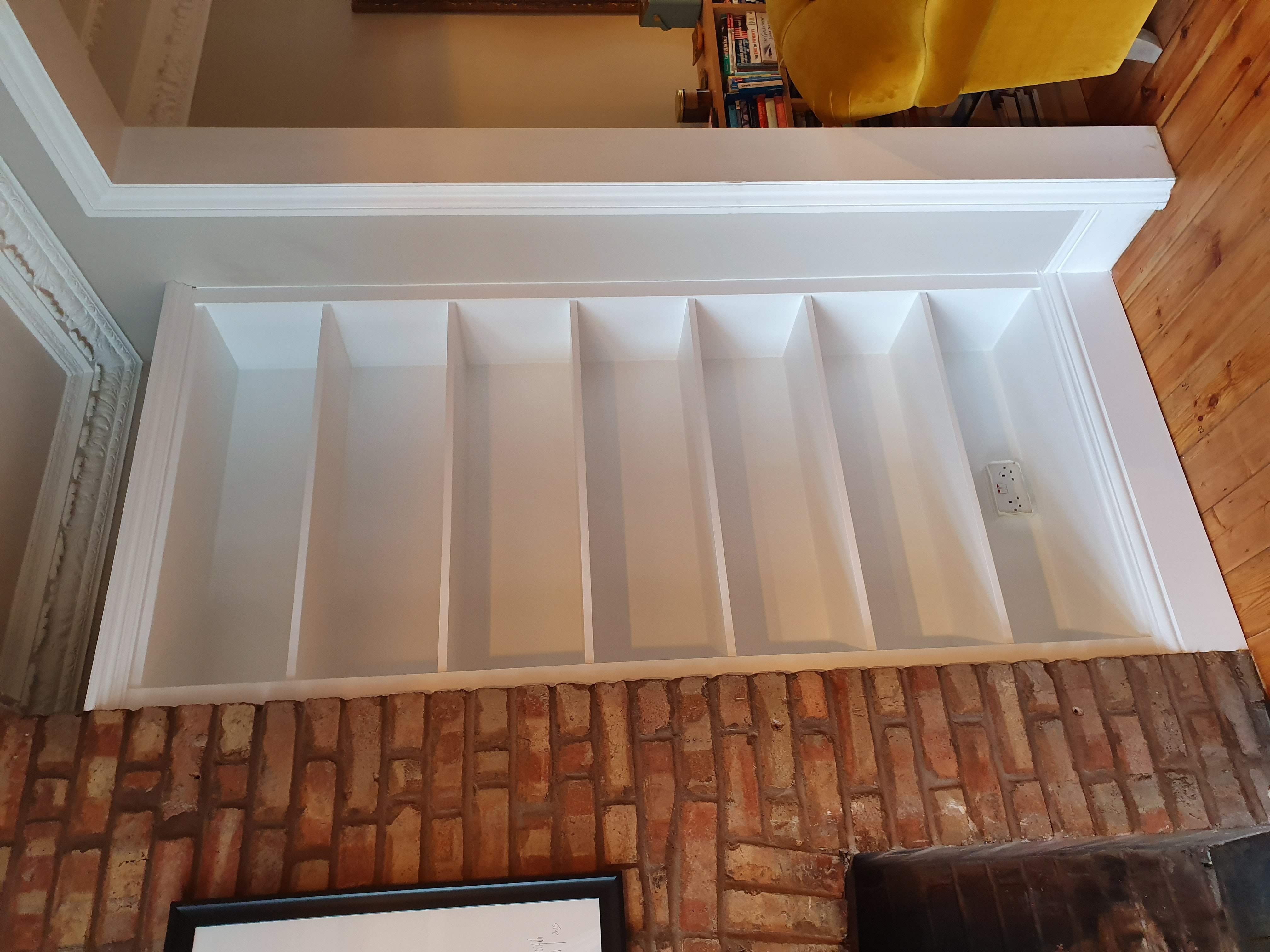 Traditional white alcove shelving unit in a living room, nestled beside a brick fireplace.