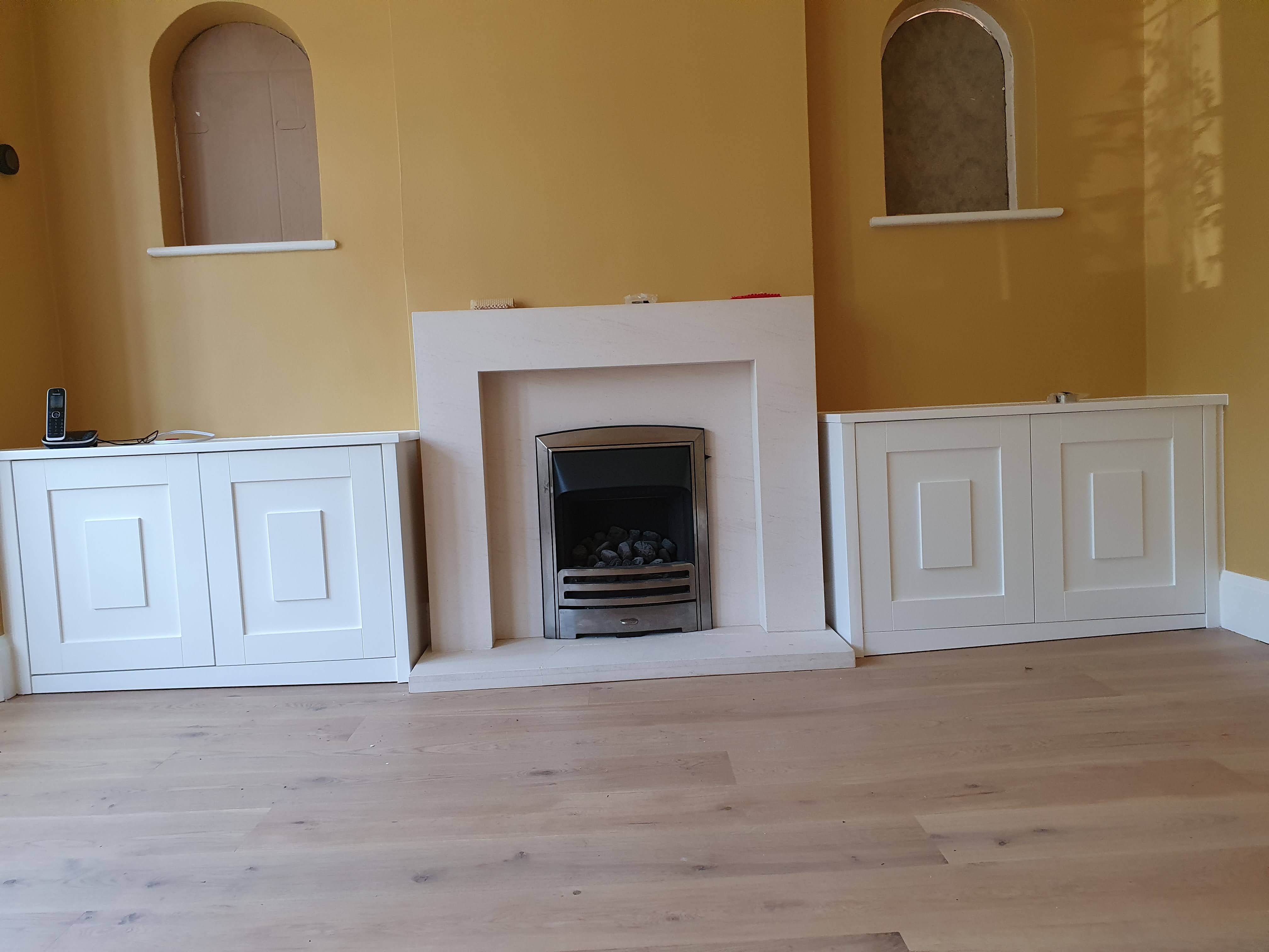 Modern white fitted media unit in a living room, featuring a TV stand, closed cabinets, and open shelving.