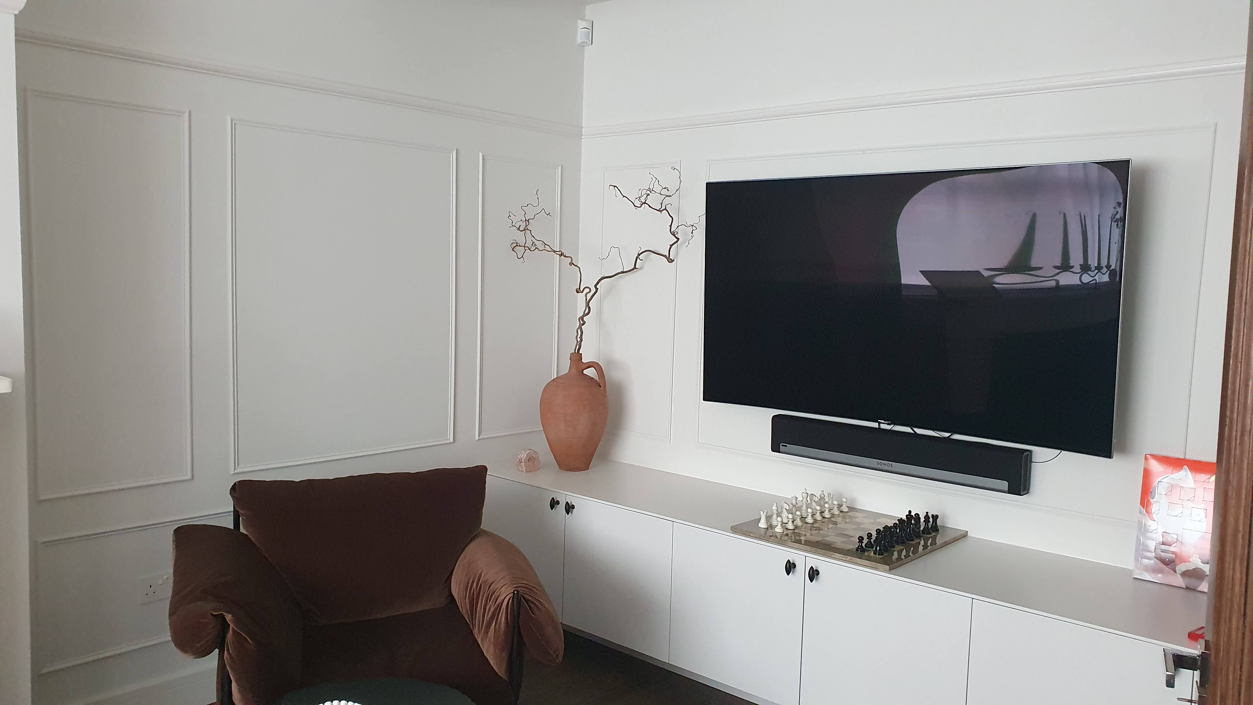 Contemporary built-in media unit in Timeless white paint for a living room, featuring paneling and black knobs.