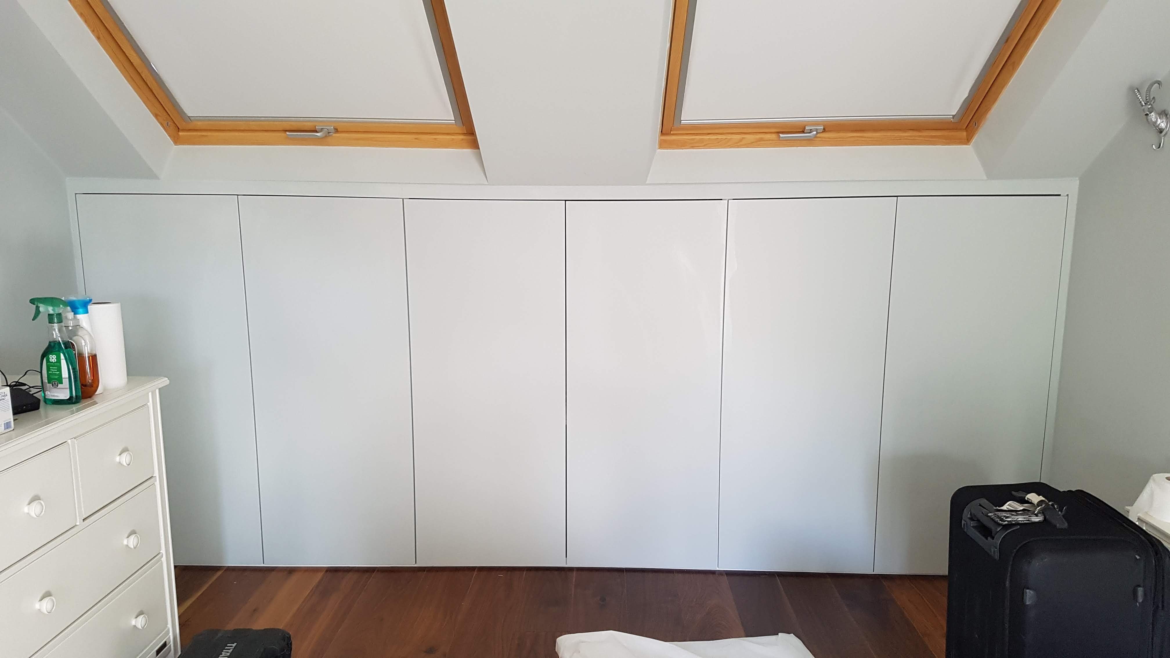 Minimalist Grey Steel fitted wardrobe in a bedroom with handleless doors, perfectly integrating with sloped ceilings.