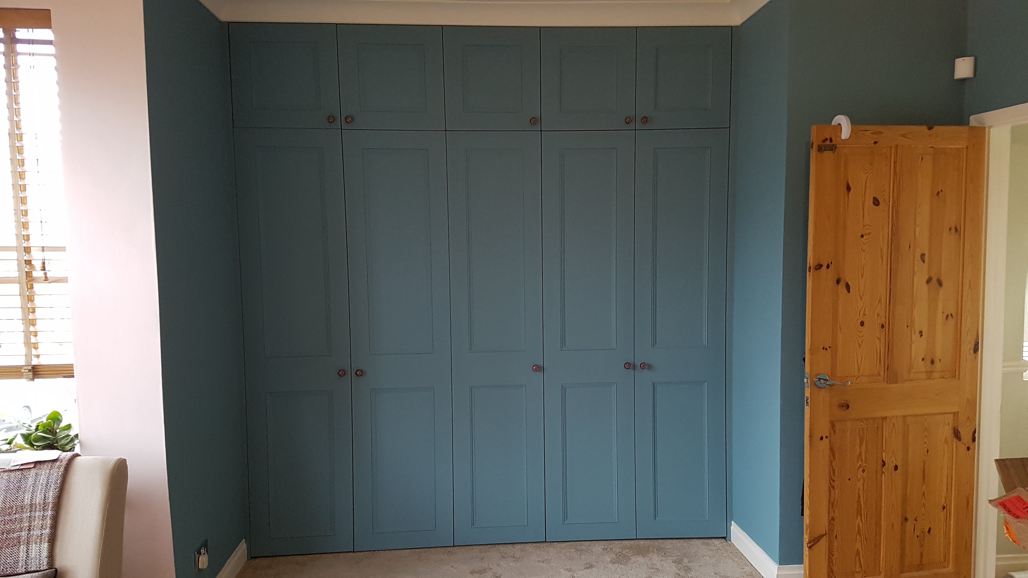 Fitted wardrobe in Farrow and Ball Hague Blue with traditional panel doors and brass knobs in a bedroom.