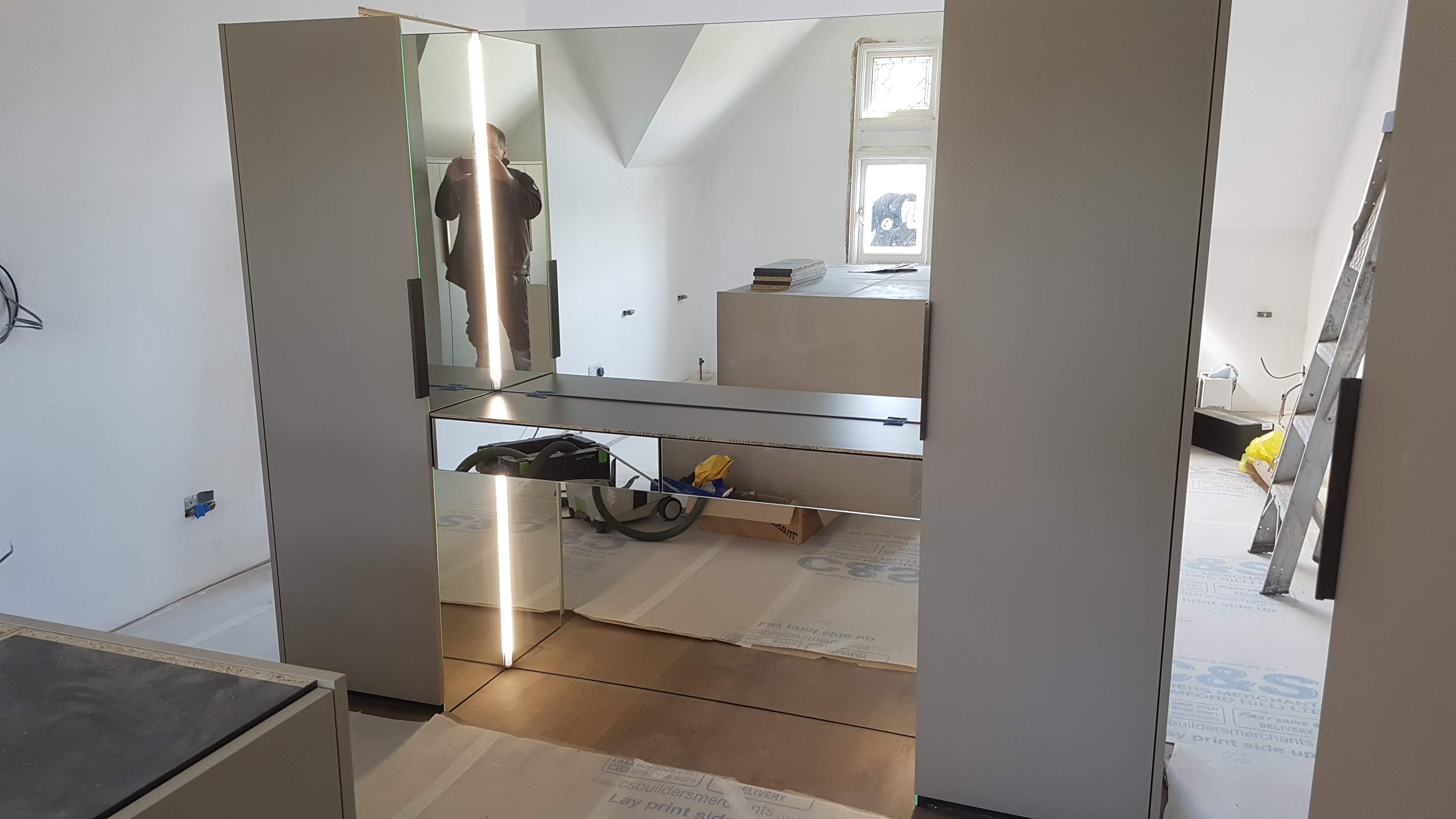 Modern fitted wardrobe in Elephant's Breath color with mirrored doors and integrated lighting for a bedroom.