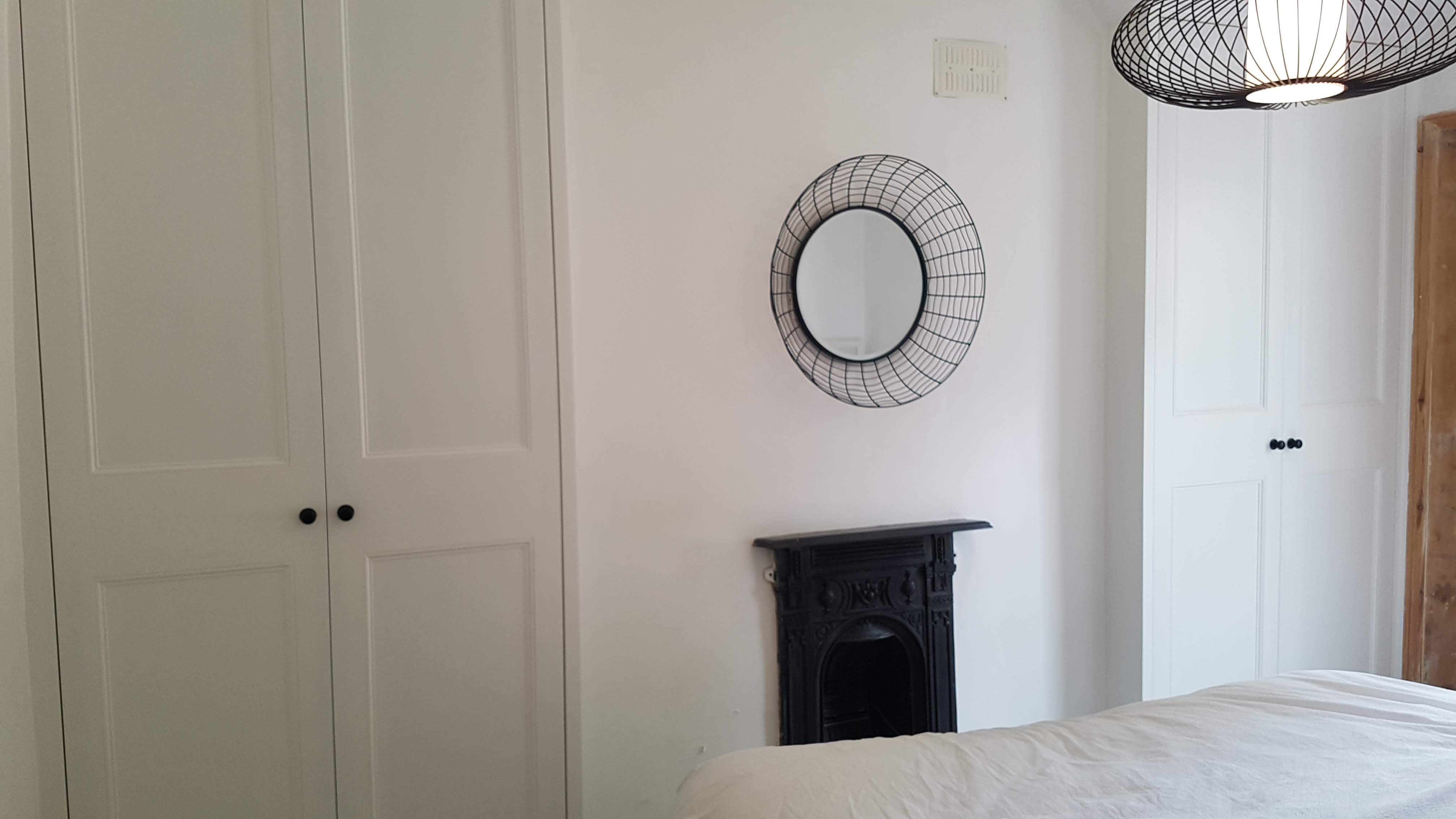 Fitted wardrobe in Shaded White Farrow and Ball paint, traditional shaker style, located in a bedroom with black knobs.