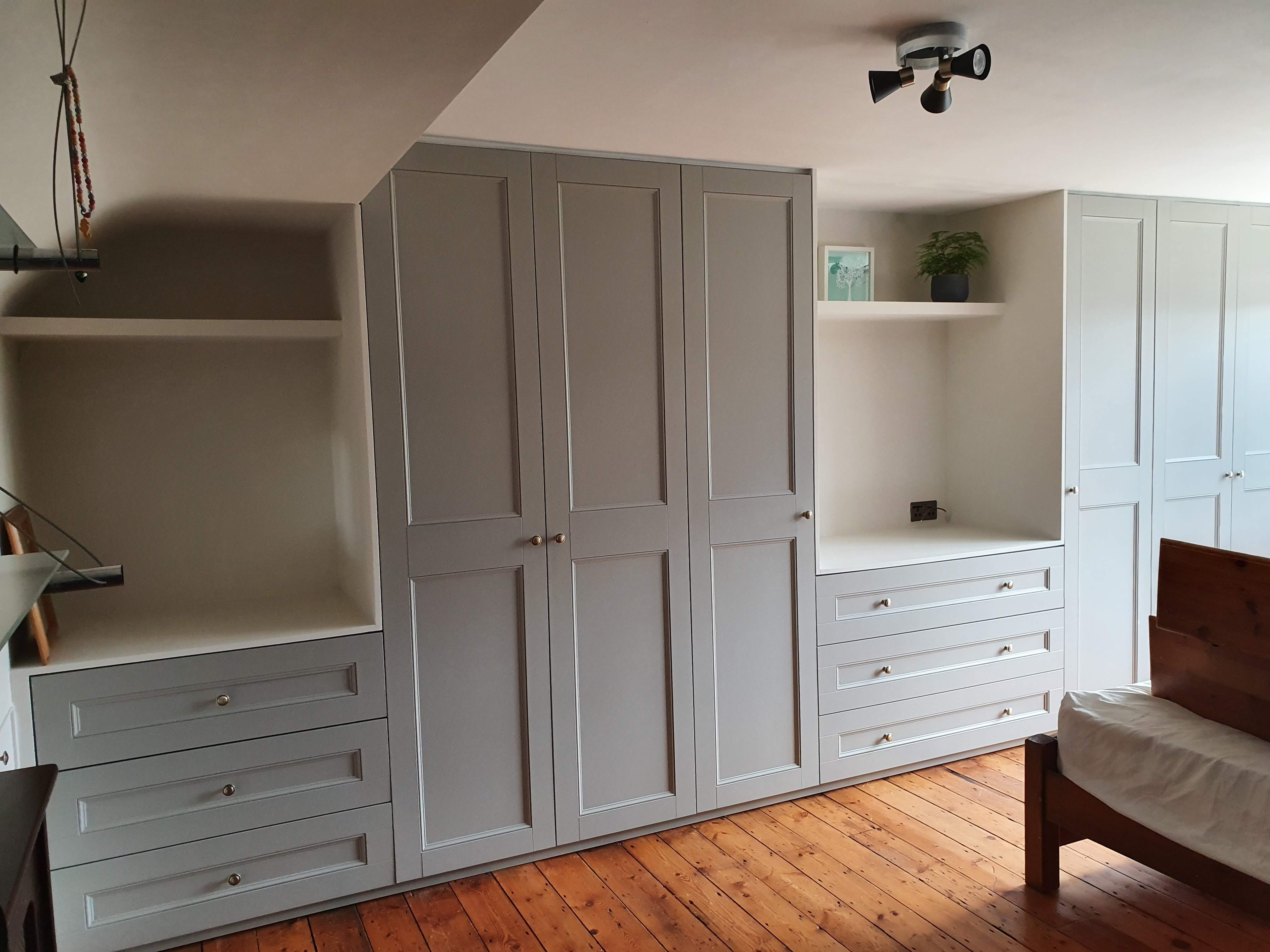 Shaker style fitted wardrobe in French Grey and Slaked Lime, featuring brass knobs, designed for a bedroom with an angled ceiling.