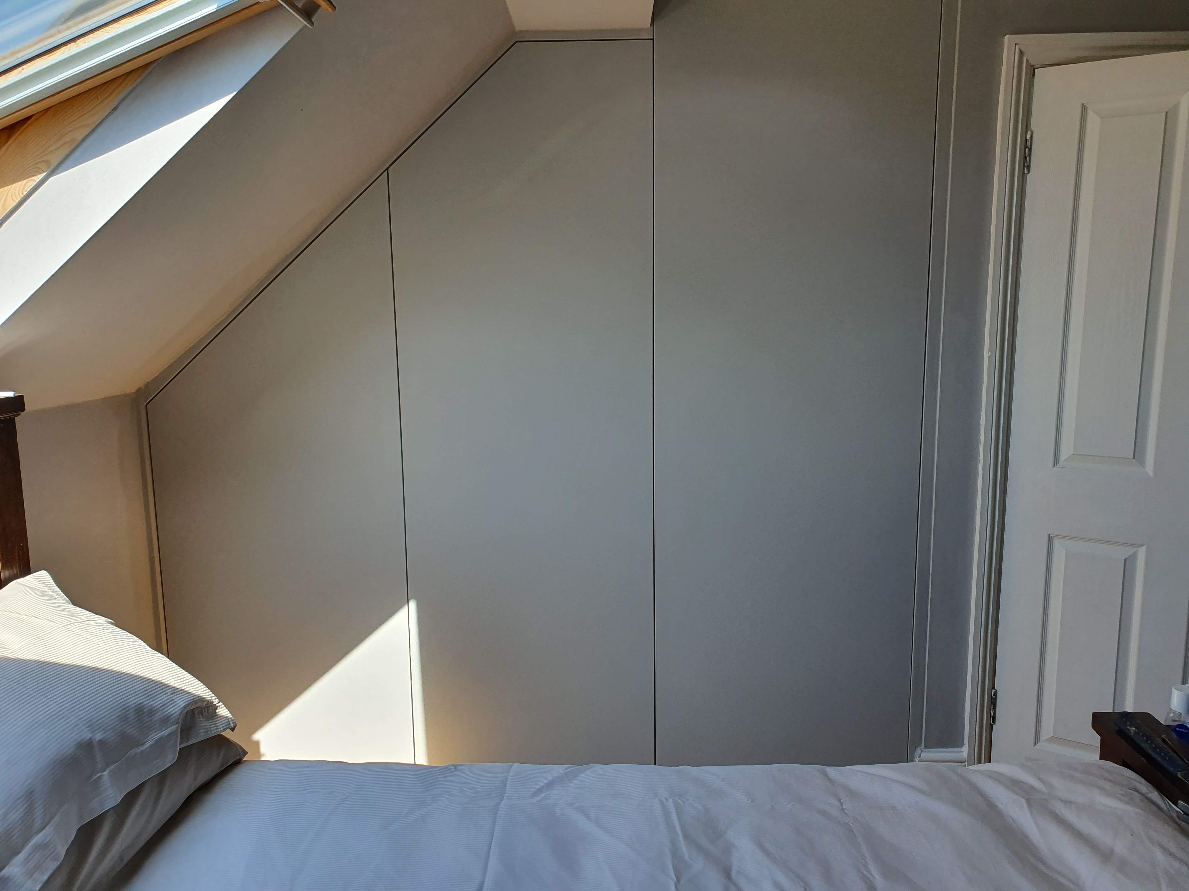 Modern fitted wardrobe in Slaked Lime Mid color, designed for a sloped ceiling bedroom with push-to-open doors.