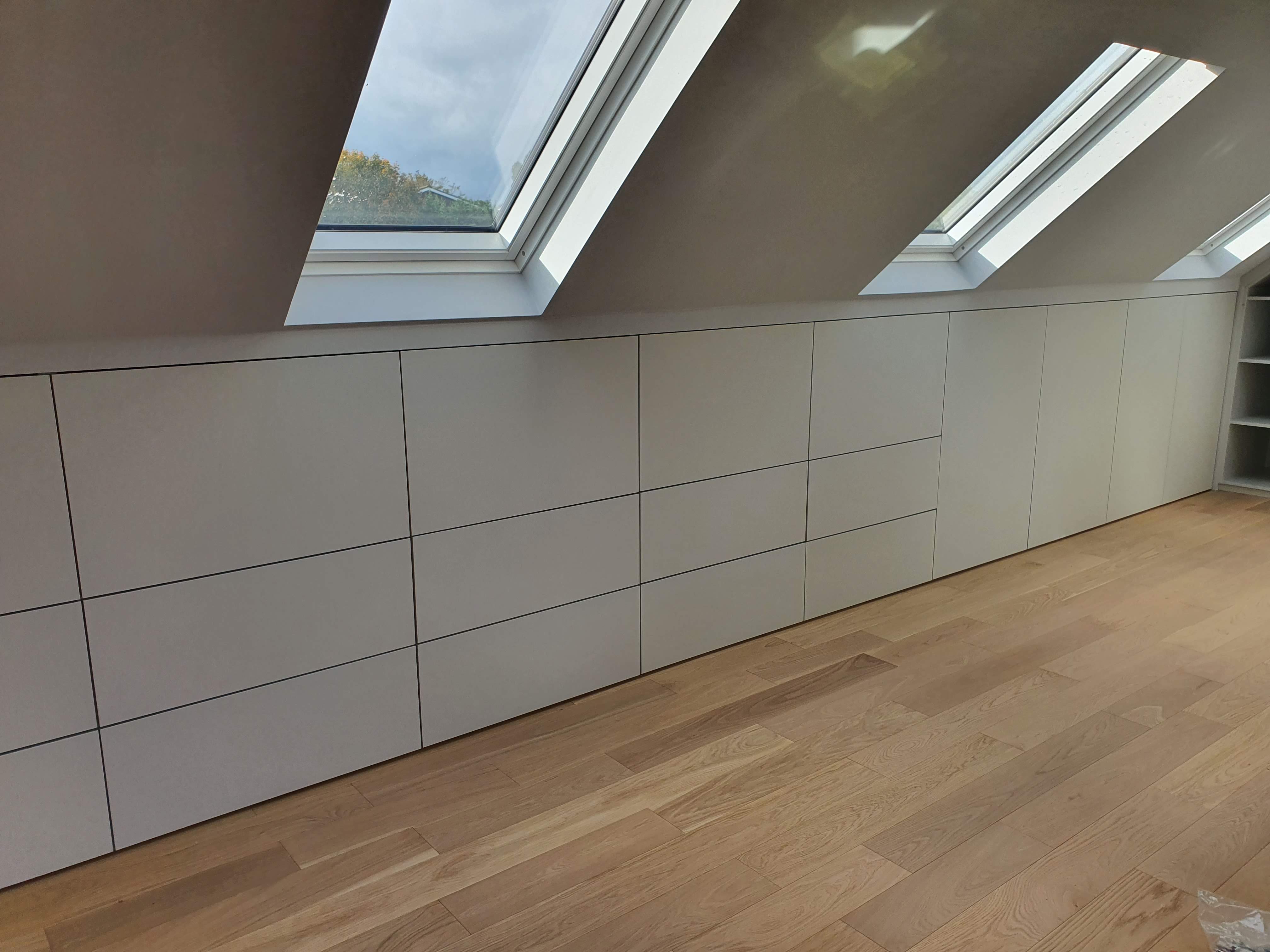 Minimalist Strong White fitted wardrobes in an attic bedroom with sloped ceilings and skylights, featuring push-to-open doors.