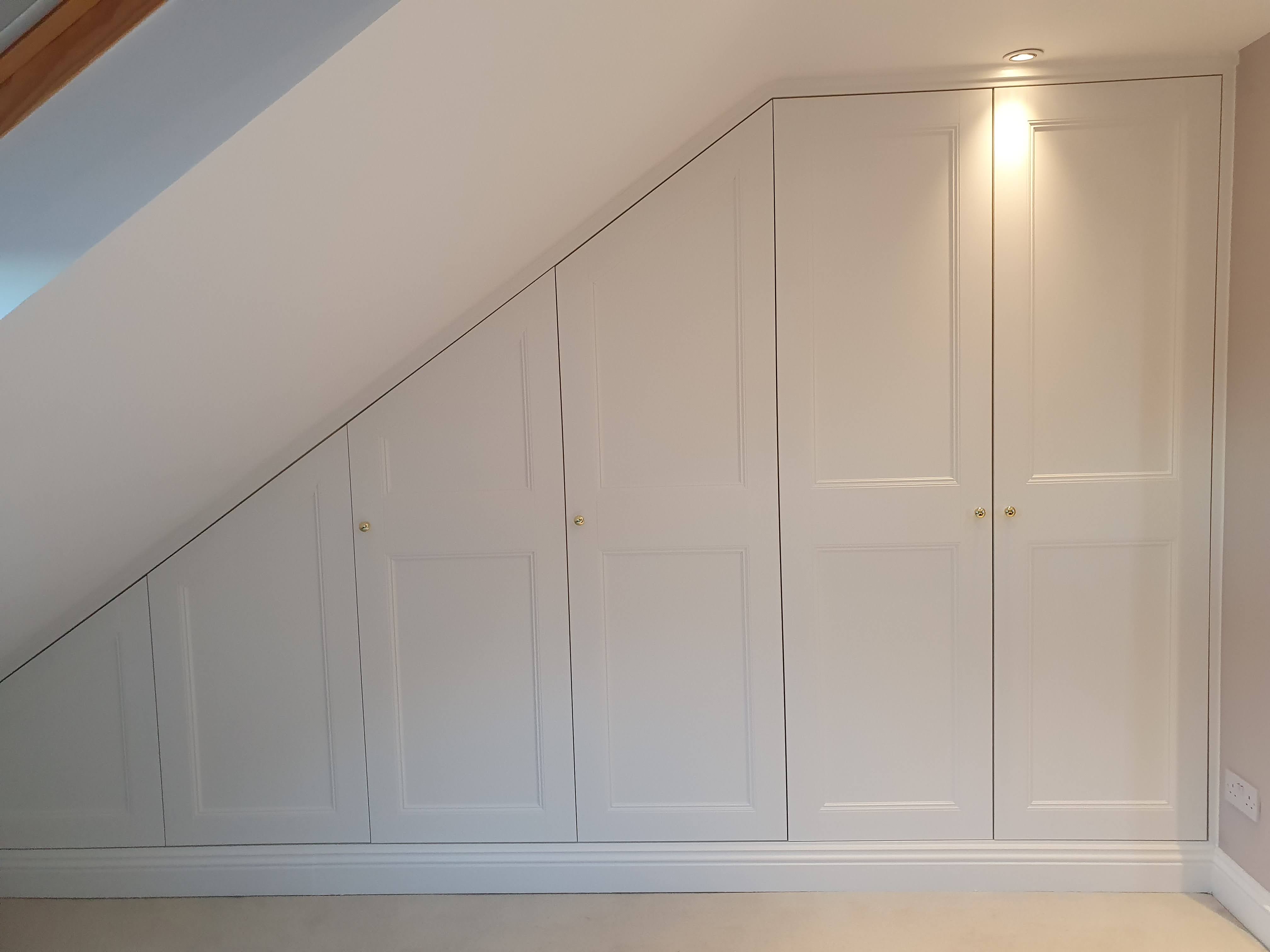 Traditional fitted wardrobe in Slaked Lime paint with brass knobs, designed for a sloped ceiling bedroom.