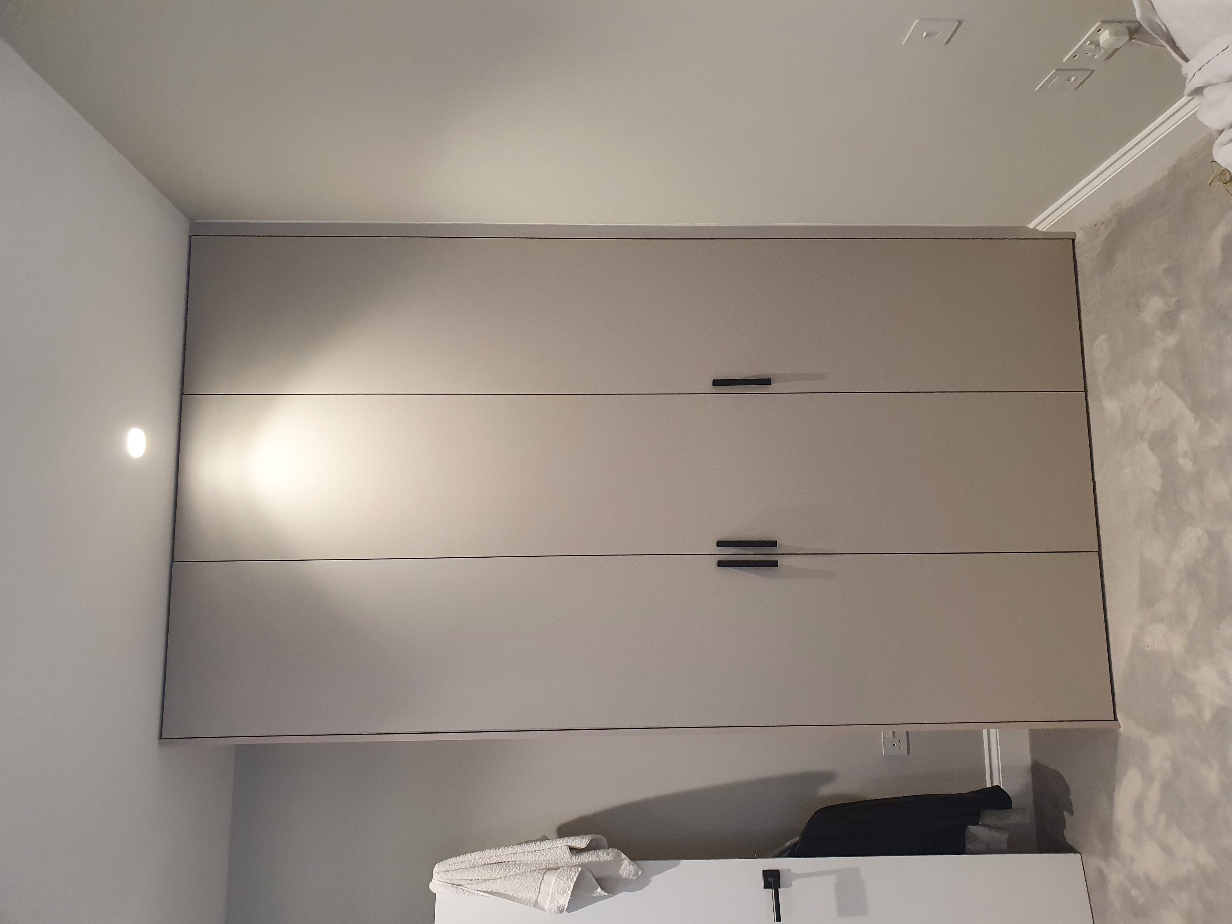 Modern fitted wardrobe in Skimming Stone color with matte black handles, perfect for a bedroom.