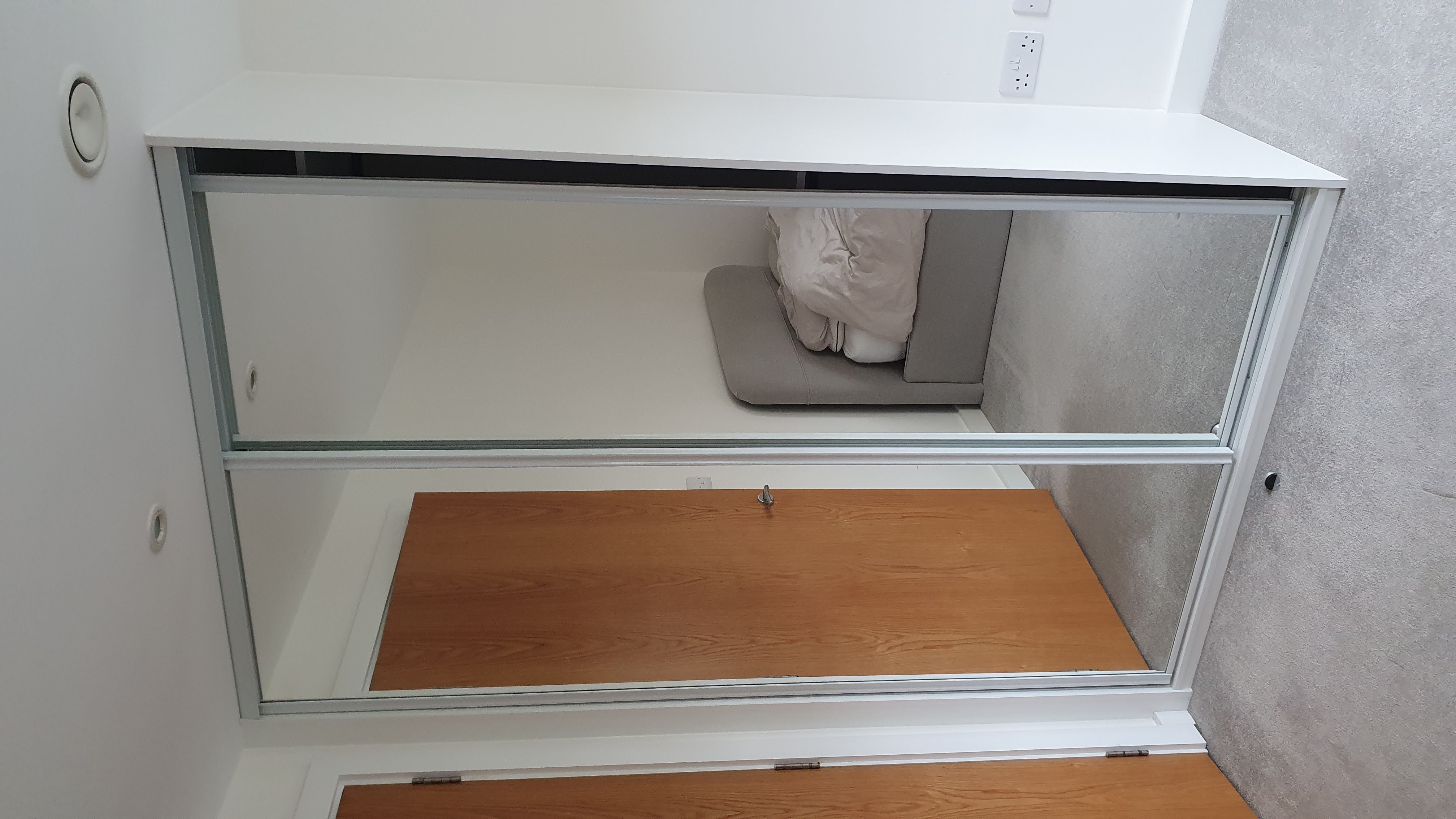 Modern white fitted wardrobe with sliding mirrored doors in a bedroom.