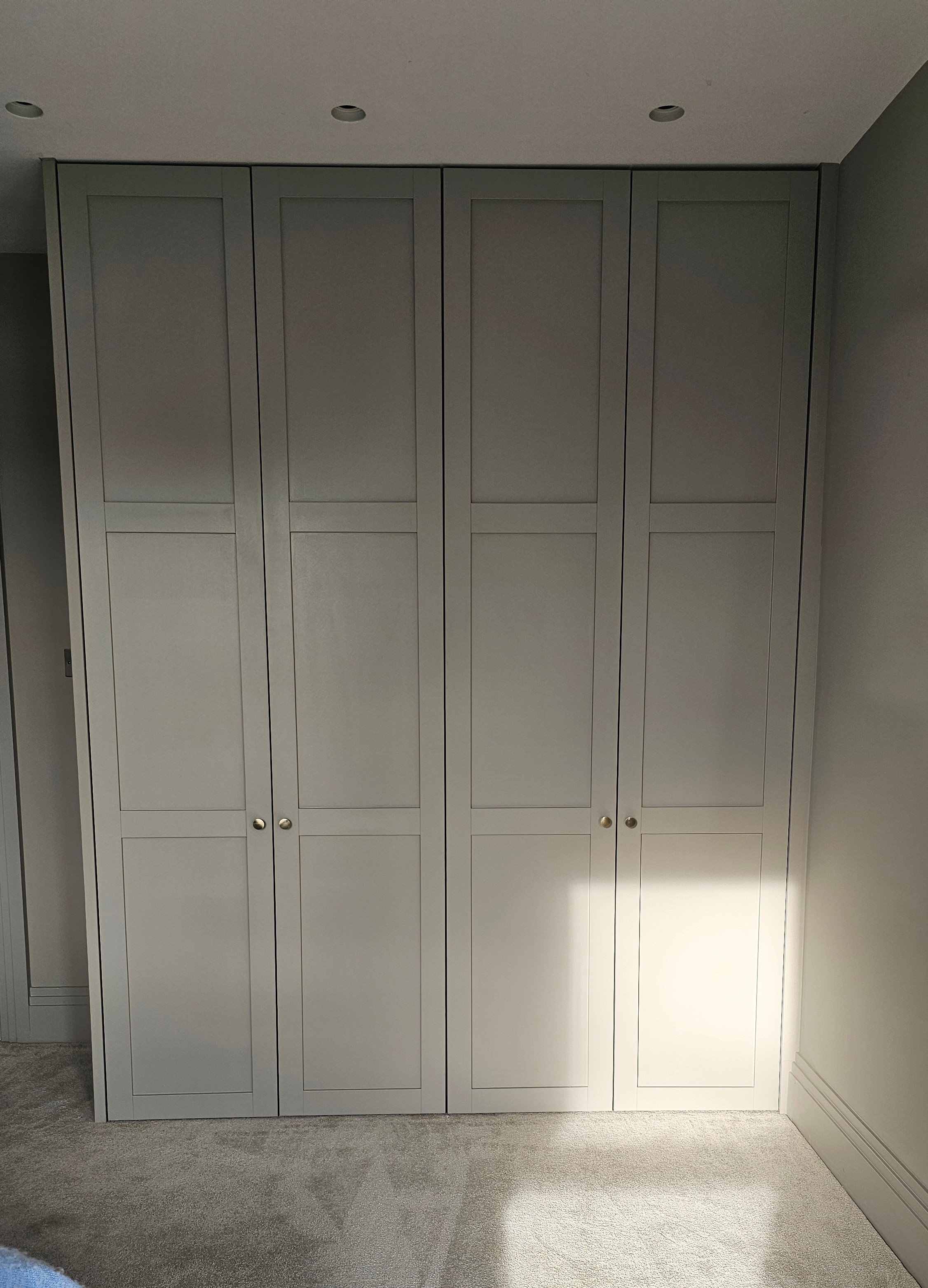 Fitted Shaker wardrobe in Skimming Stone by Farrow and Ball, with brass knobs, ideal for a modern bedroom.