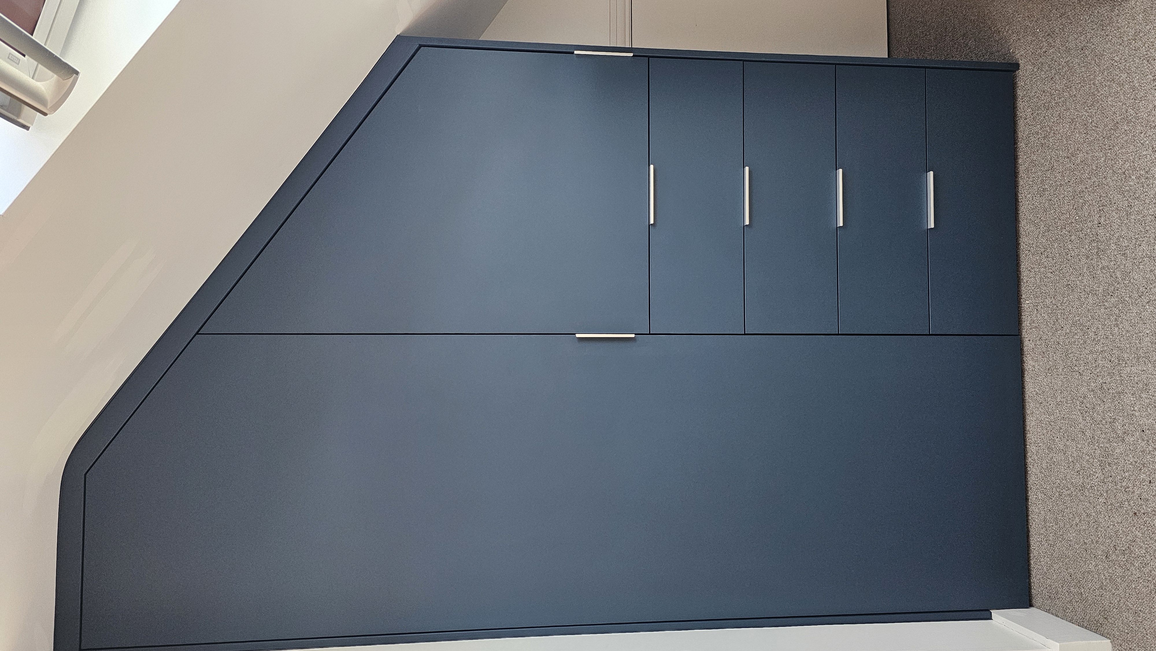 Contemporary Hague Blue fitted wardrobe with integrated drawers, designed for a sloping ceiling in a modern bedroom.