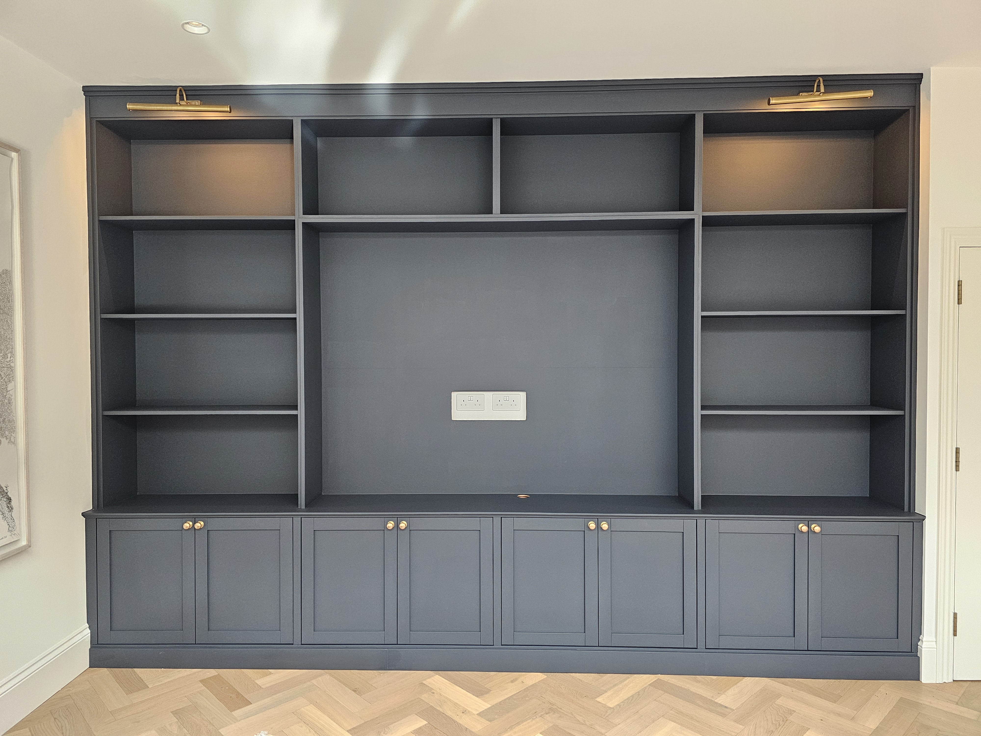 Beautiful Shaker style fitted bookcase in deep Hague Blue, featuring ample shelving and lower cabinets with elegant brass knobs, perfect for a contemporary living room.