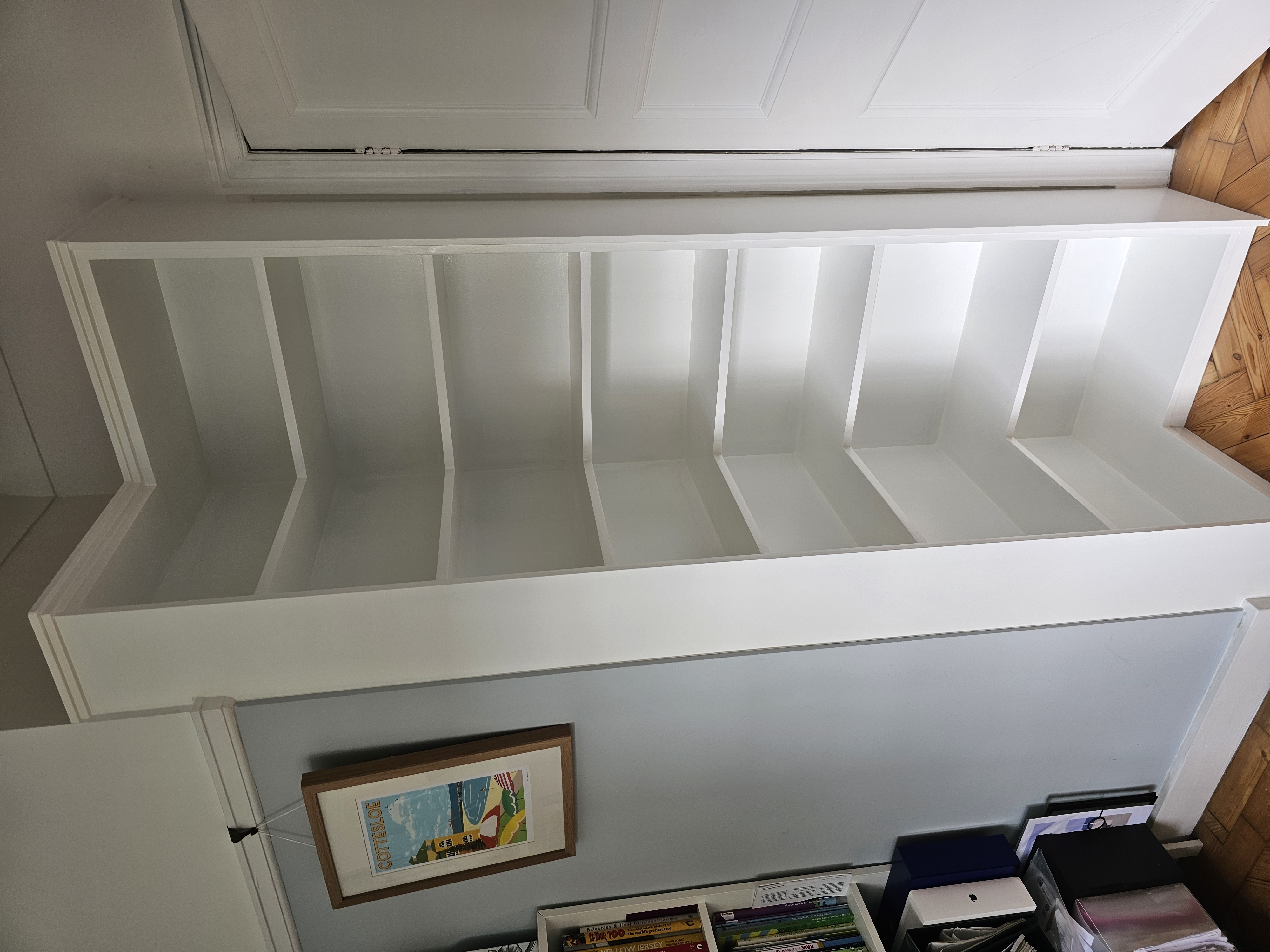 Contemporary white fitted corner bookcase in a hallway, offering open shelving for storage.