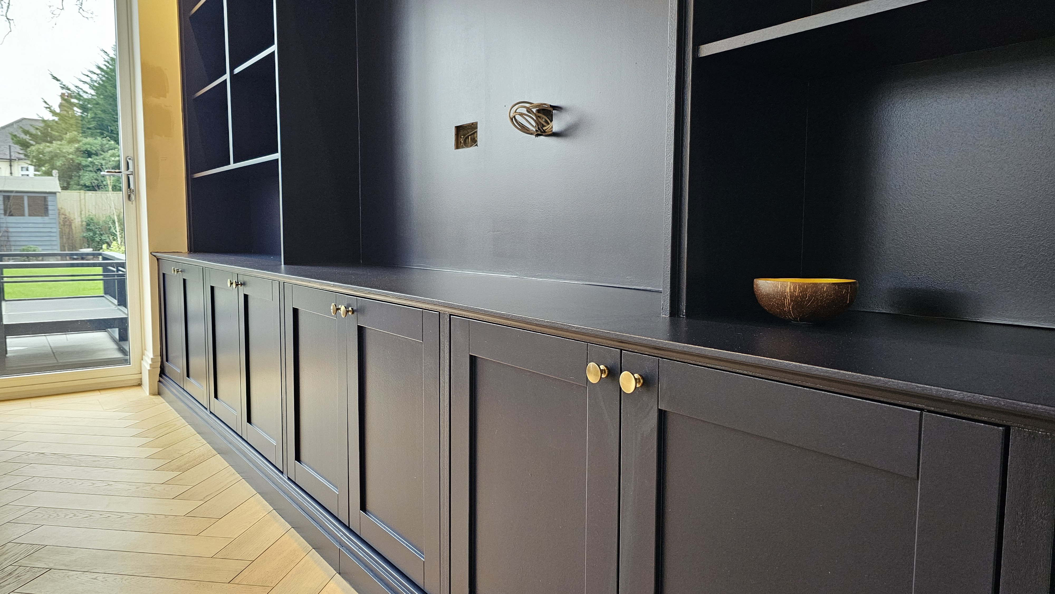 Dark blue Shaker style built-in storage unit in a living room, with brass knobs and open shelving.