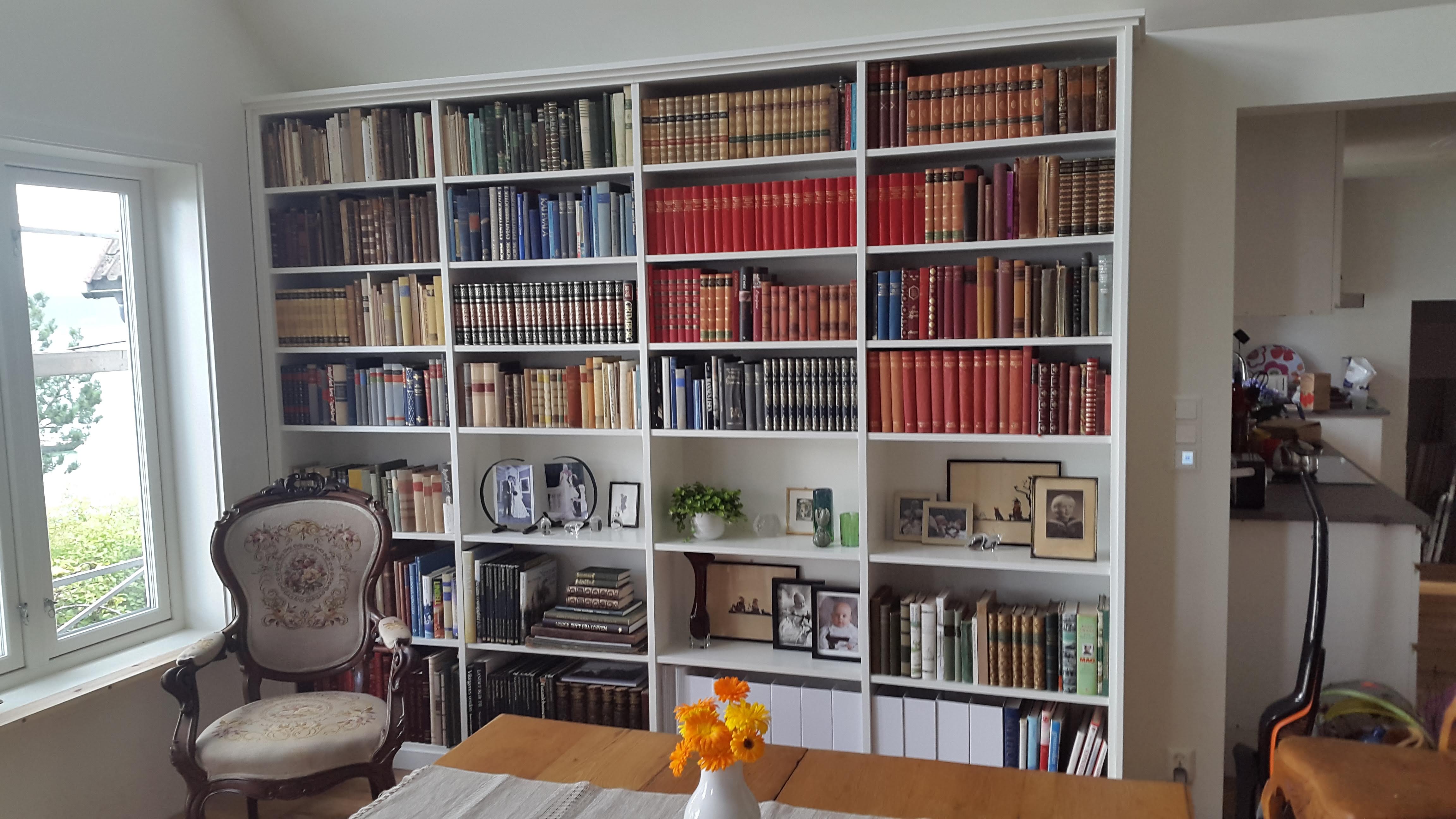 Traditional fitted bookcase in Timeless white paint, extending across a living room wall, filled with books and decorative items.
